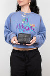 Person wearing a blue sweatshirt , holding a black wallet against a plain background