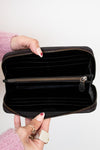 Black wallet held open by a hand with pink sleeves and red nail polish on a white background