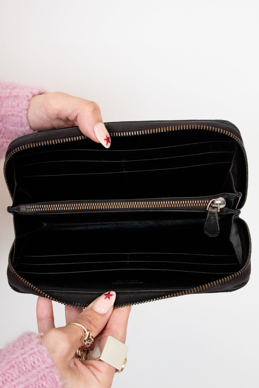 Black wallet held open by a hand with pink sleeves and red nail polish on a white background