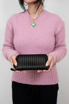 Person wearing a pink sweater holding a black wallet against a plain background