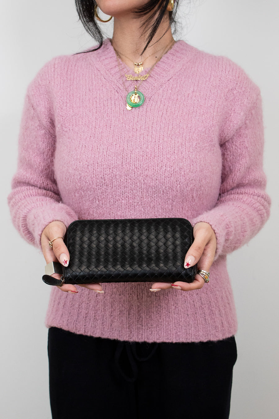 Person wearing a pink sweater holding a black wallet against a plain background