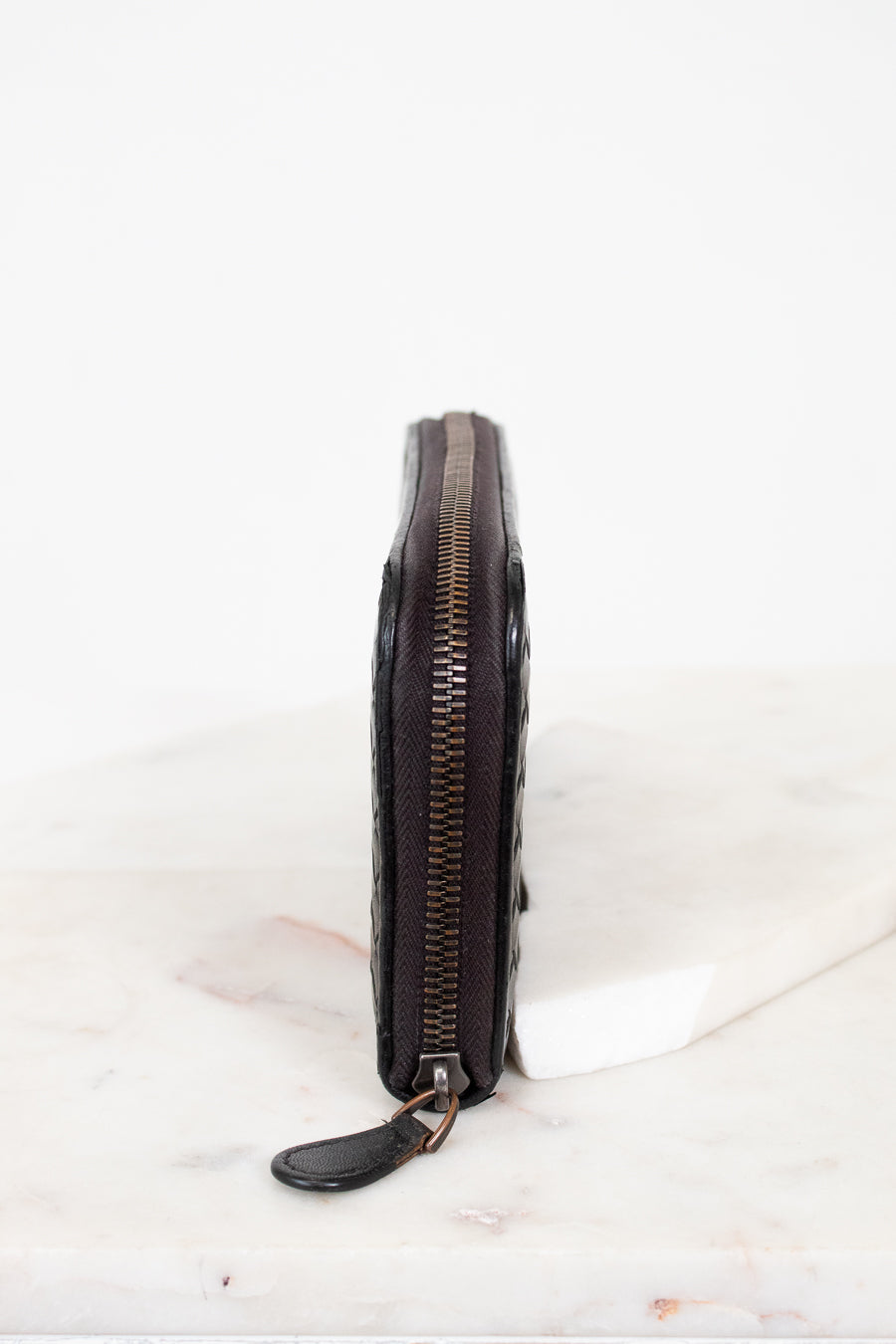 Black leather wallet with zipper on a white marble surface