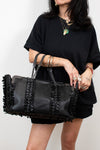 Person holding a black handbag with braided details against a plain background