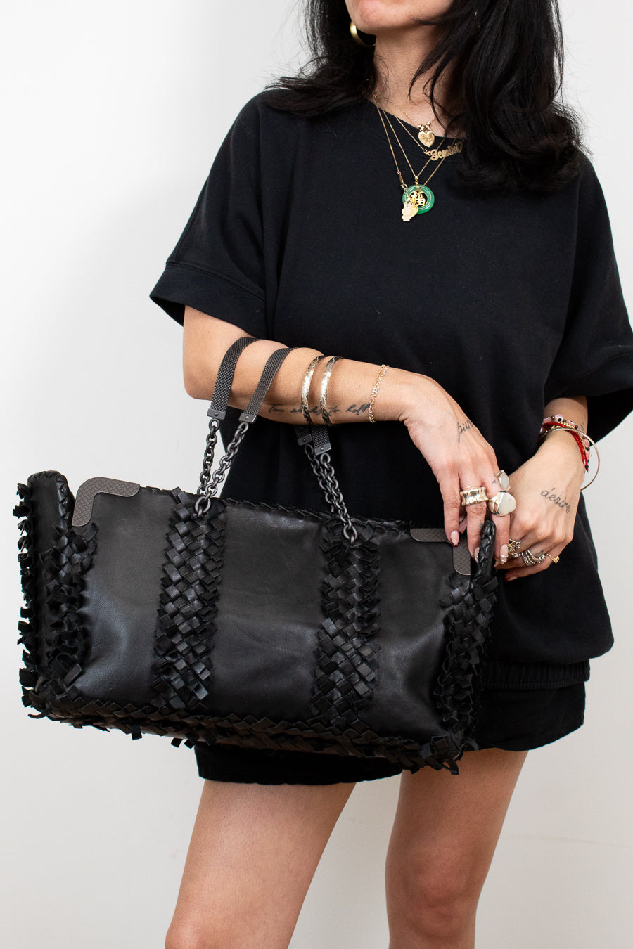 Person holding a black handbag with braided details against a plain background