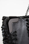 Close-up of a black woven handbag with a textured flap.