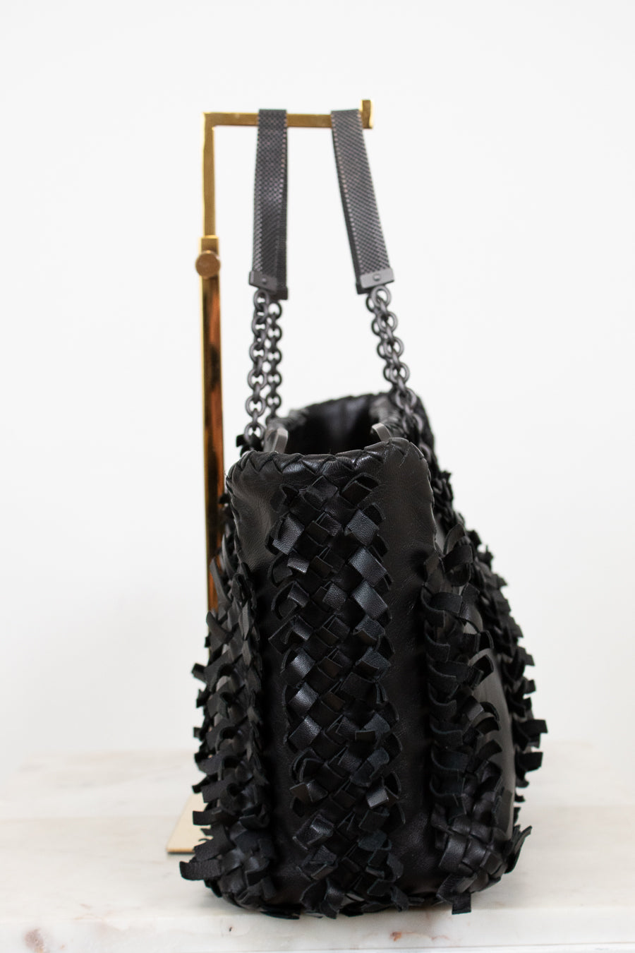 Black woven handbag with chain detail on a white background