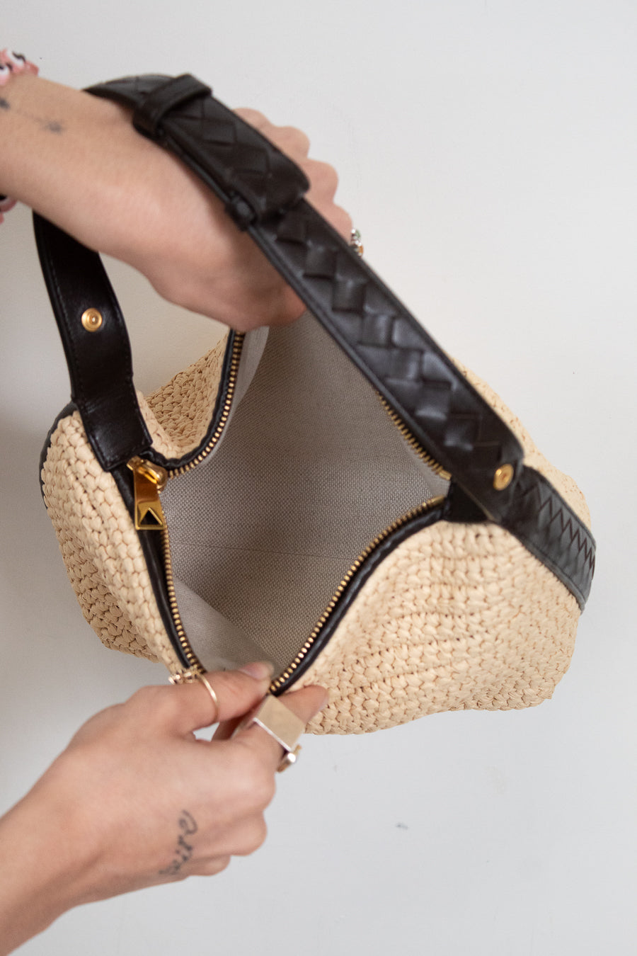 Woven handbag with black leather trim held by a person against a neutral background