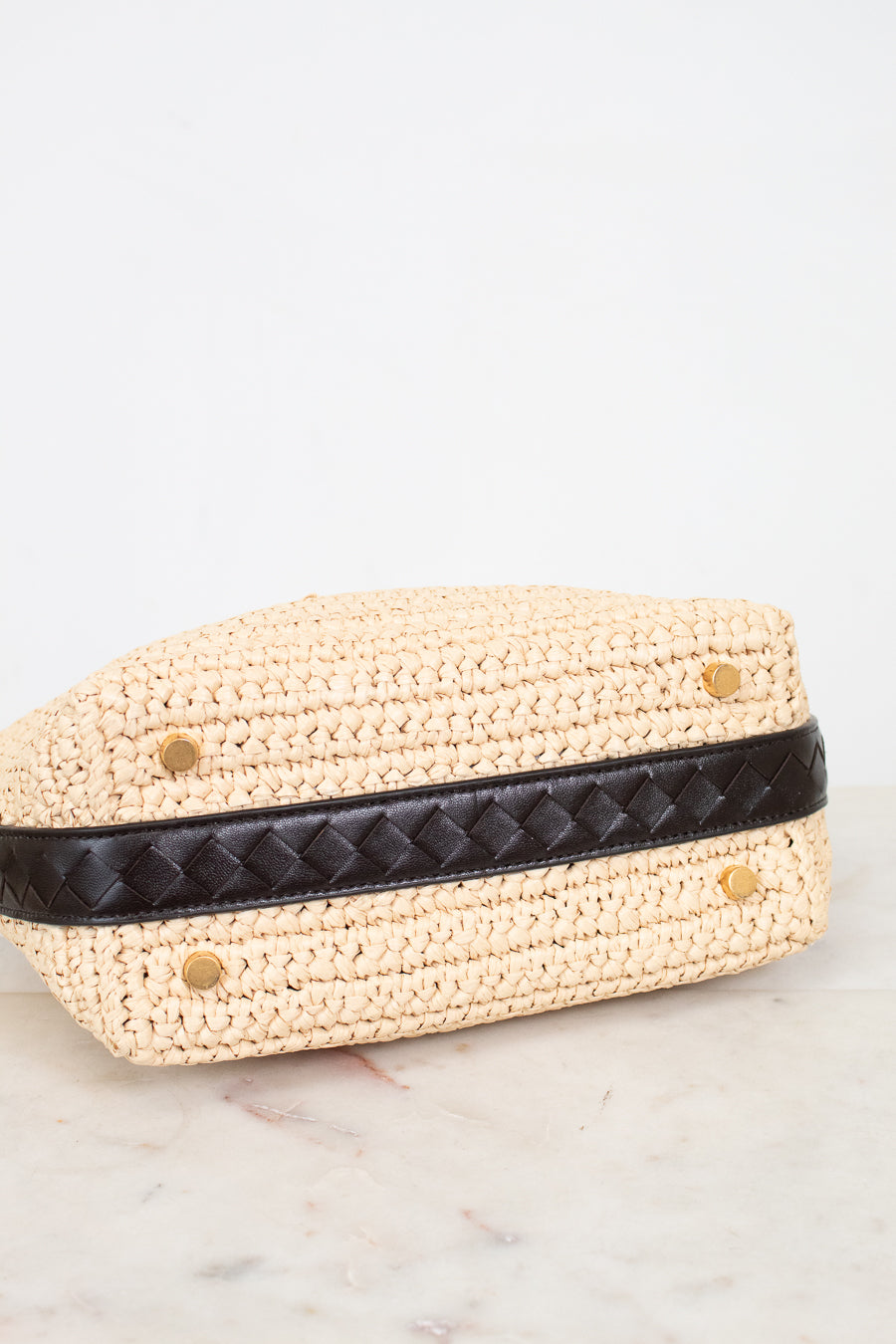 Woven beige handbag with a black strap on a marble surface