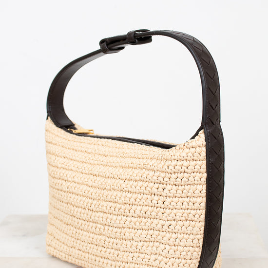 Beige woven handbag with black handle on a light gray background
