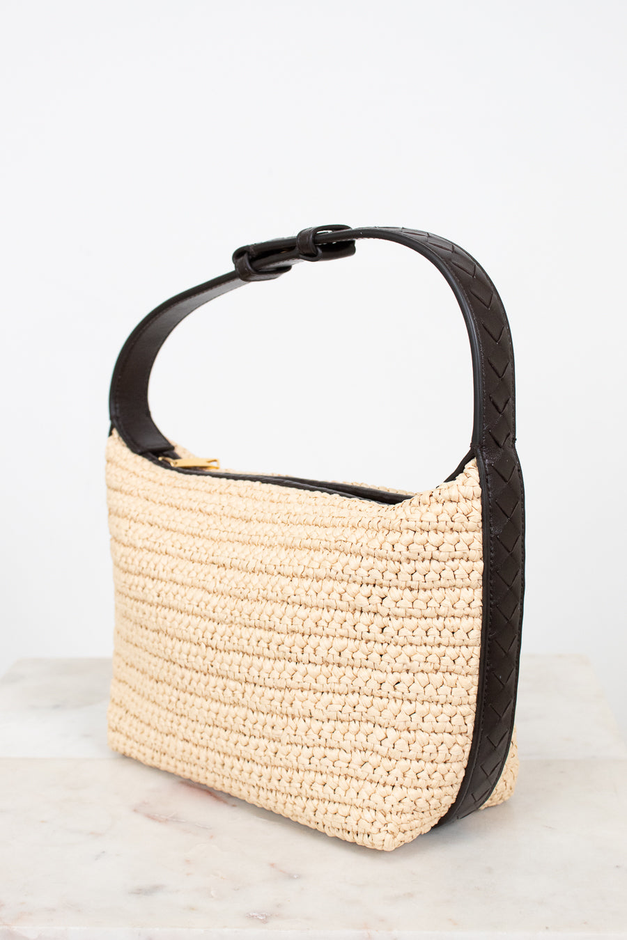 Beige woven handbag with black handle on a light gray background