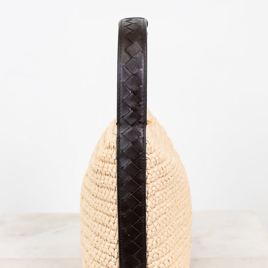 Beige woven handbag with a black handle on a white background
