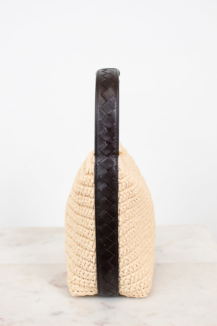 Beige woven handbag with a black handle on a white background