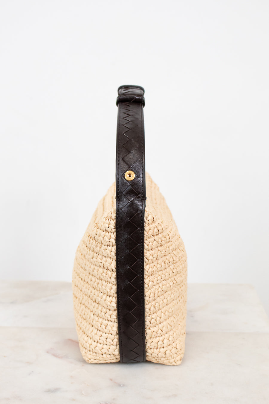 Woven handbag with a black strap on a light background