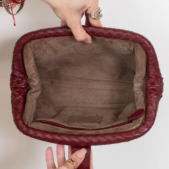 A close-up of a burgundy quilted leather handbag held open by two hands against a plain white background, showing a brown suede-like interior lining.