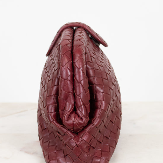 A burgundy woven leather handbag shown from the back, resting on a light marble surface against a white background.