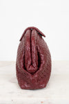 A burgundy woven leather handbag shown from the back, resting on a light marble surface against a white background.