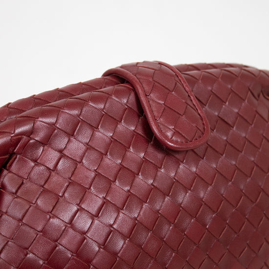A close-up of a woven leather bag in deep burgundy, showing the detailed basketweave texture and a matching leather snap closure against a plain white background.