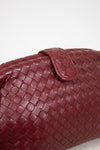 A close-up of a woven leather bag in deep burgundy, showing the detailed basketweave texture and a matching leather snap closure against a plain white background.