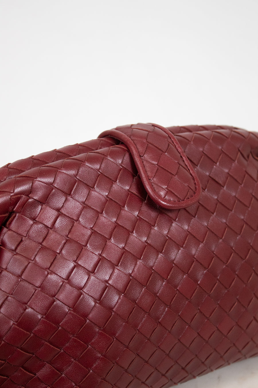 A close-up of a woven leather bag in deep burgundy, showing the detailed basketweave texture and a matching leather snap closure against a plain white background.