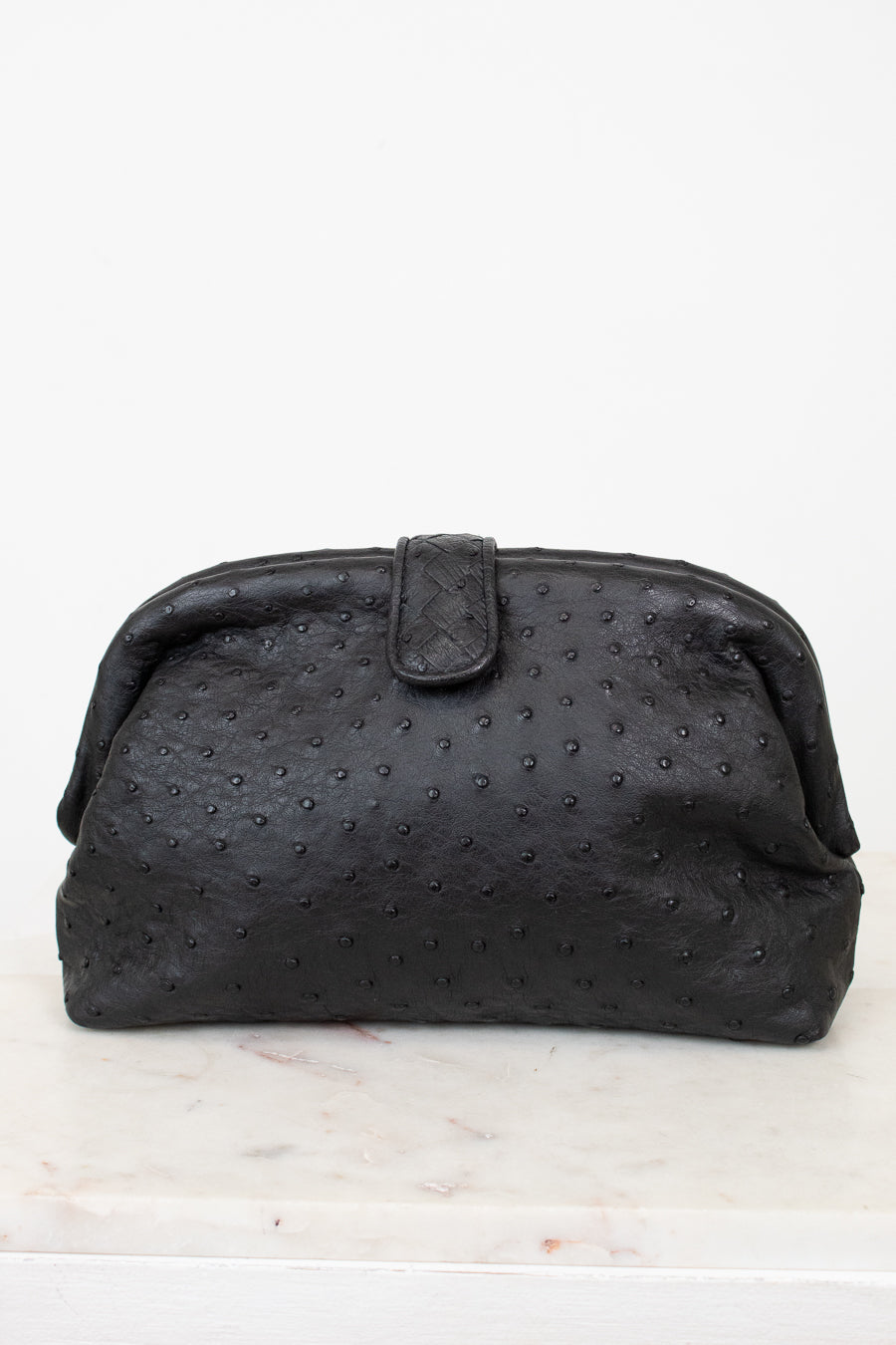 Black textured clutch bag on a white marble surface