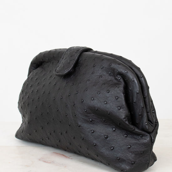 Black textured clutch bag on a light marble surface with a white background