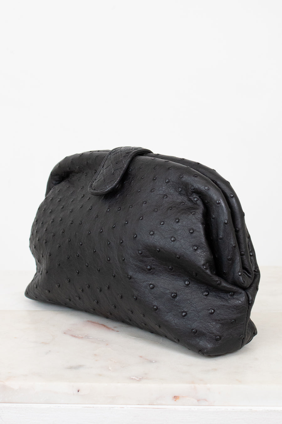 Black textured clutch bag on a light marble surface with a white background