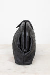 Side view of black ostrich-patterned handbag on a light gray background