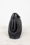 Side view of black ostrich-patterned handbag on a light gray background