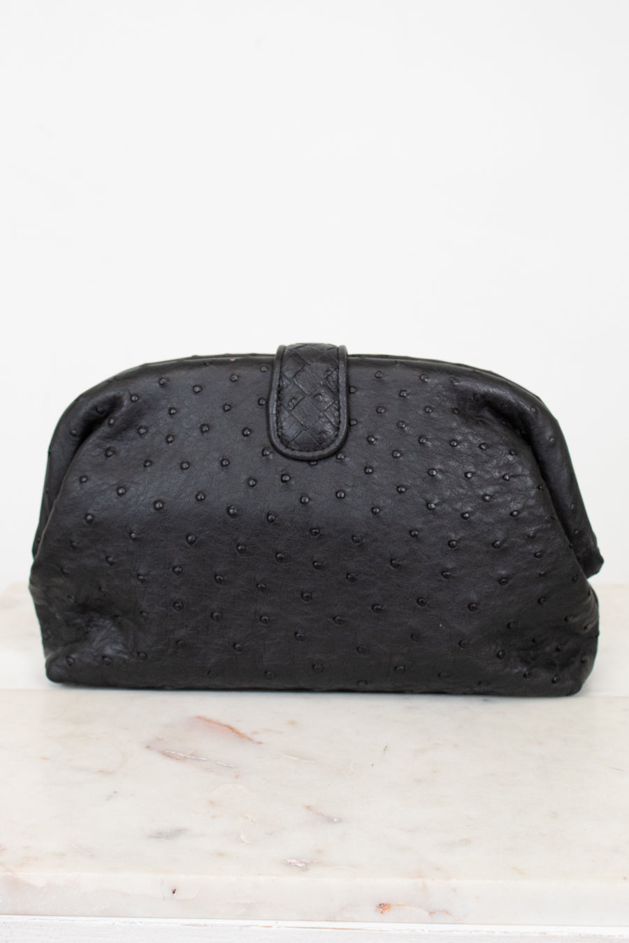 Black textured clutch bag on a white marble surface