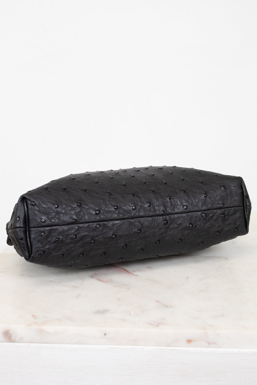 Black ostrich-patterned clutch bag on a light marble surface