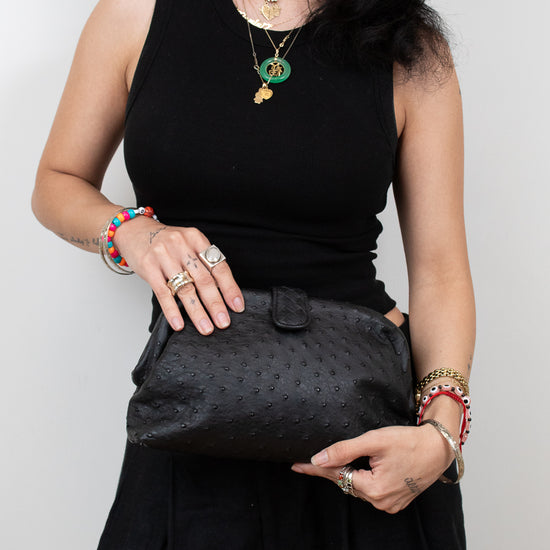 Woman holding a black textured clutch against a plain background