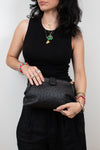Woman holding a black textured clutch against a plain background