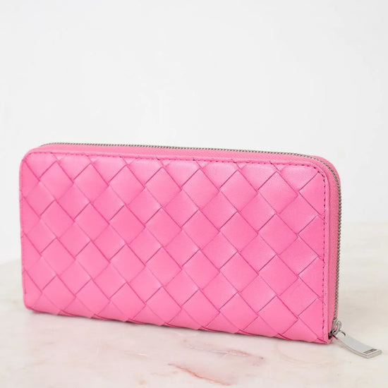 Pink quilted wallet on a light pink surface with a white background