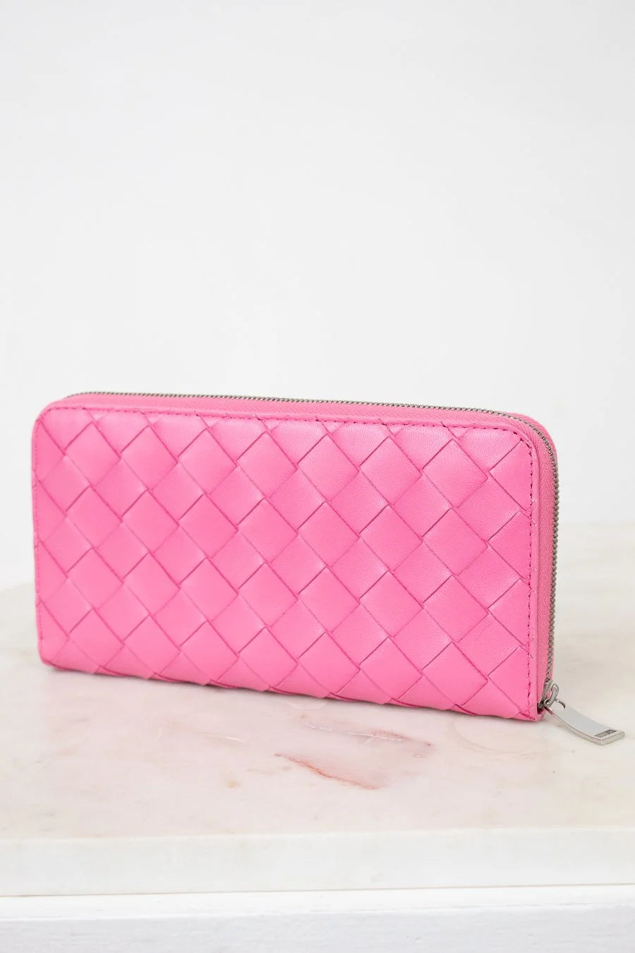 Pink quilted wallet on a light pink surface with a white background