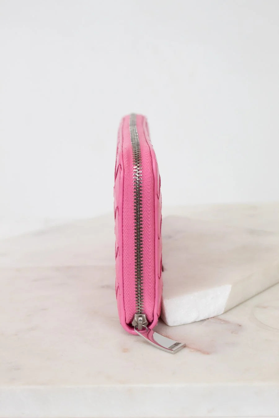Pink wallet side profile with a zipper on a light marble surface