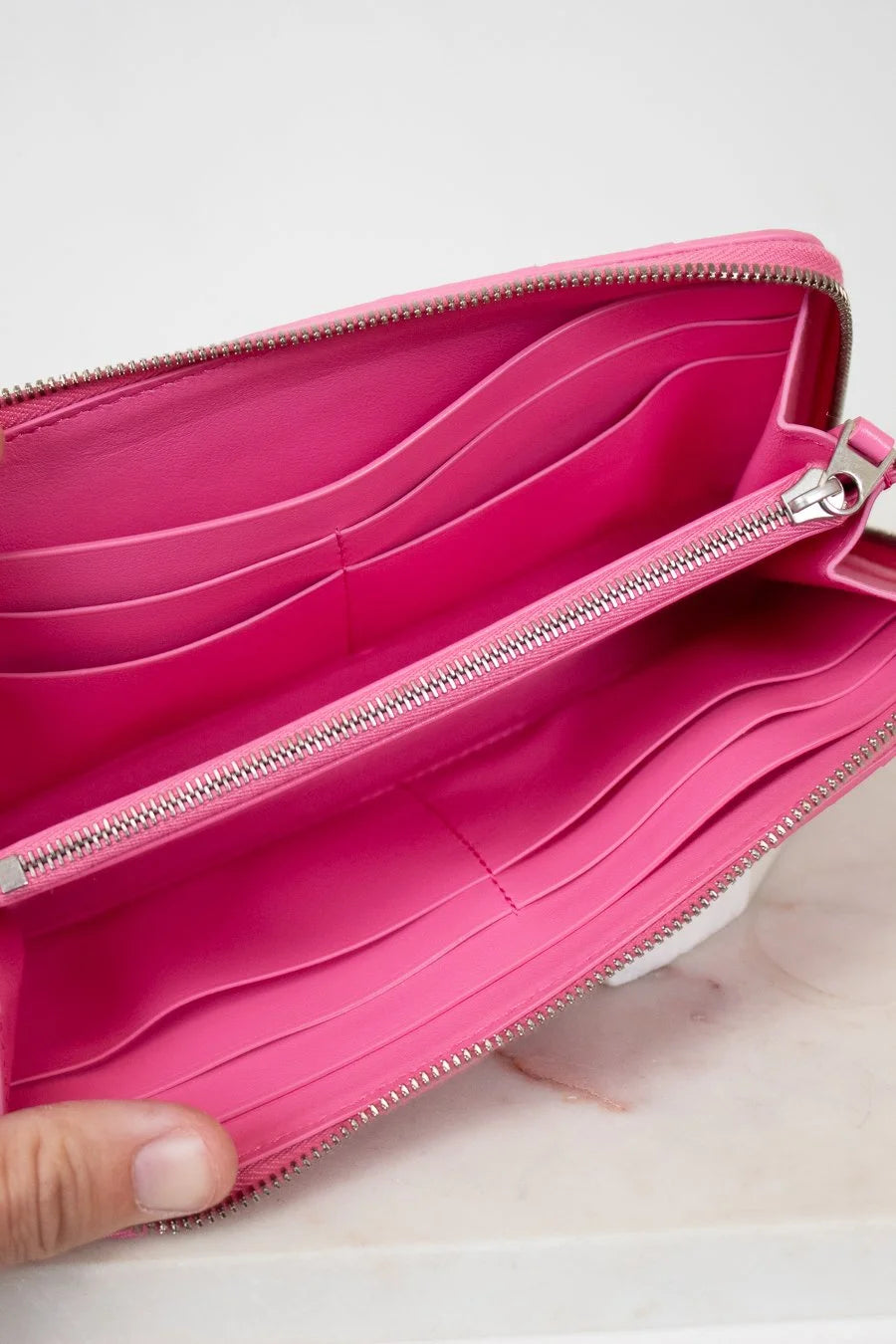 Pink wallet with a hand holding it open on a light background