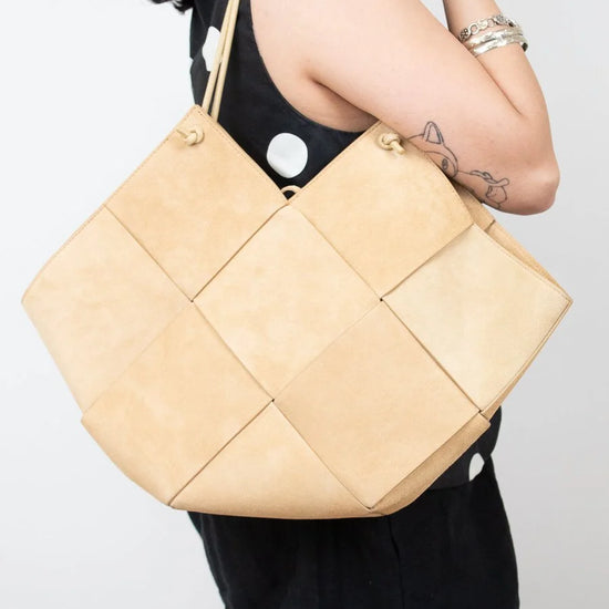 Beige quilted handbag held by a person against a white background