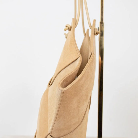 Beige handbag hanging on a gold stand against a white background
