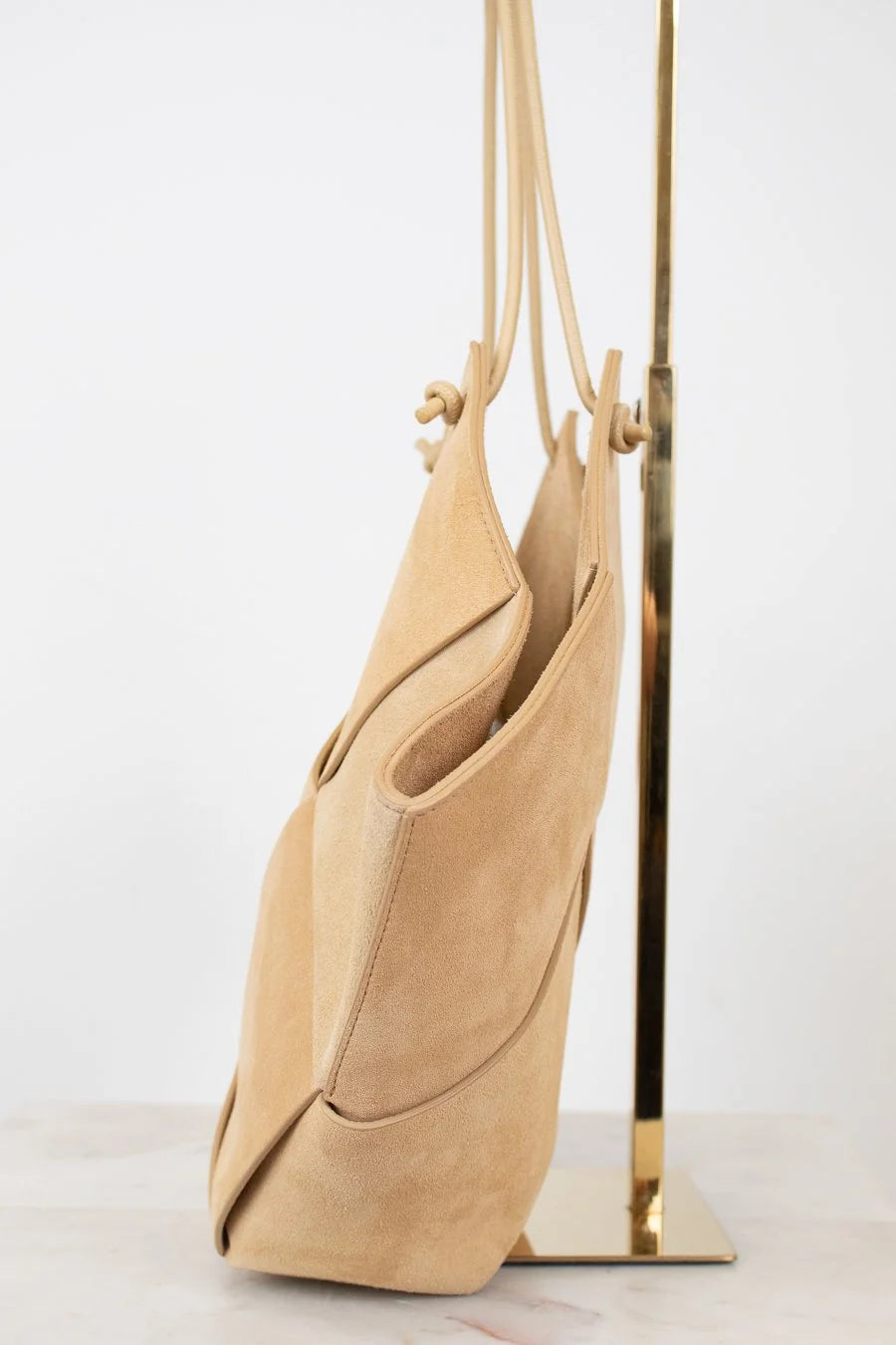 Beige handbag hanging on a gold stand against a white background