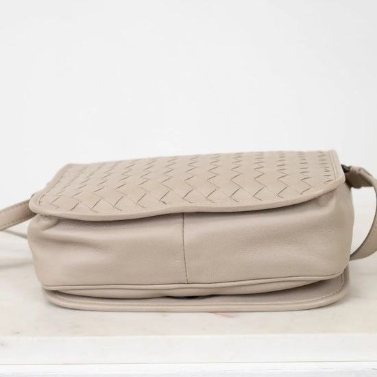 Beige woven handbag on a white surface with a white background