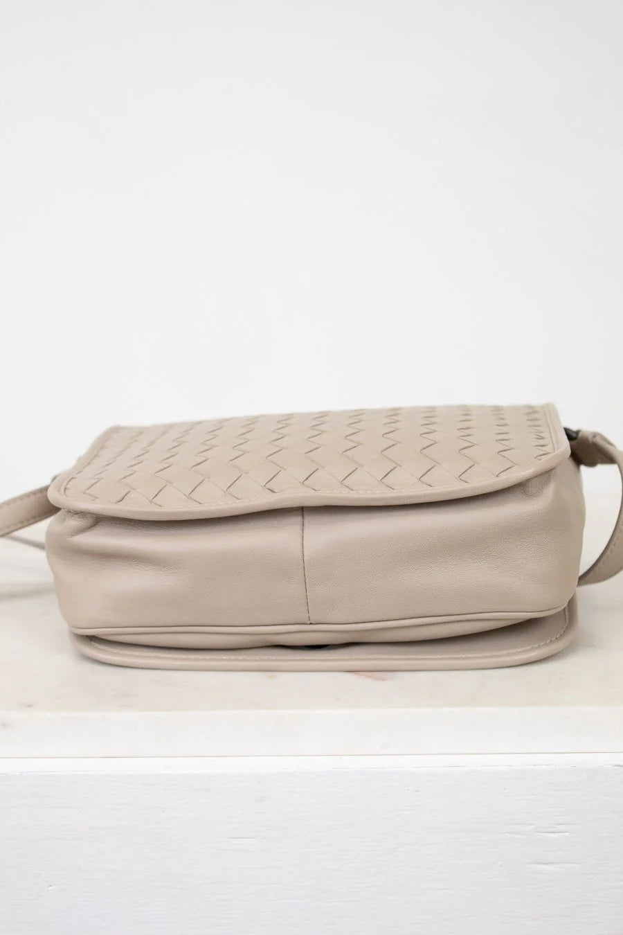 Beige woven handbag on a white surface with a white background