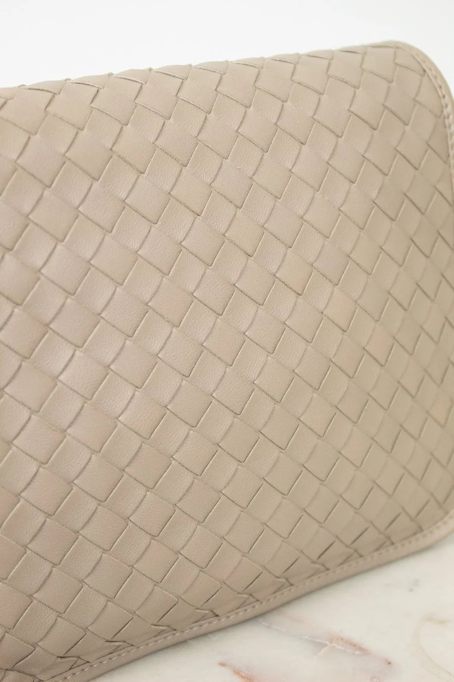 Beige woven clutch bag on a light marble background
