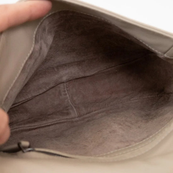 Close-up of a beige leather bag with a hand holding it open.