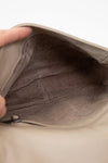 Close-up of a beige leather bag with a hand holding it open.