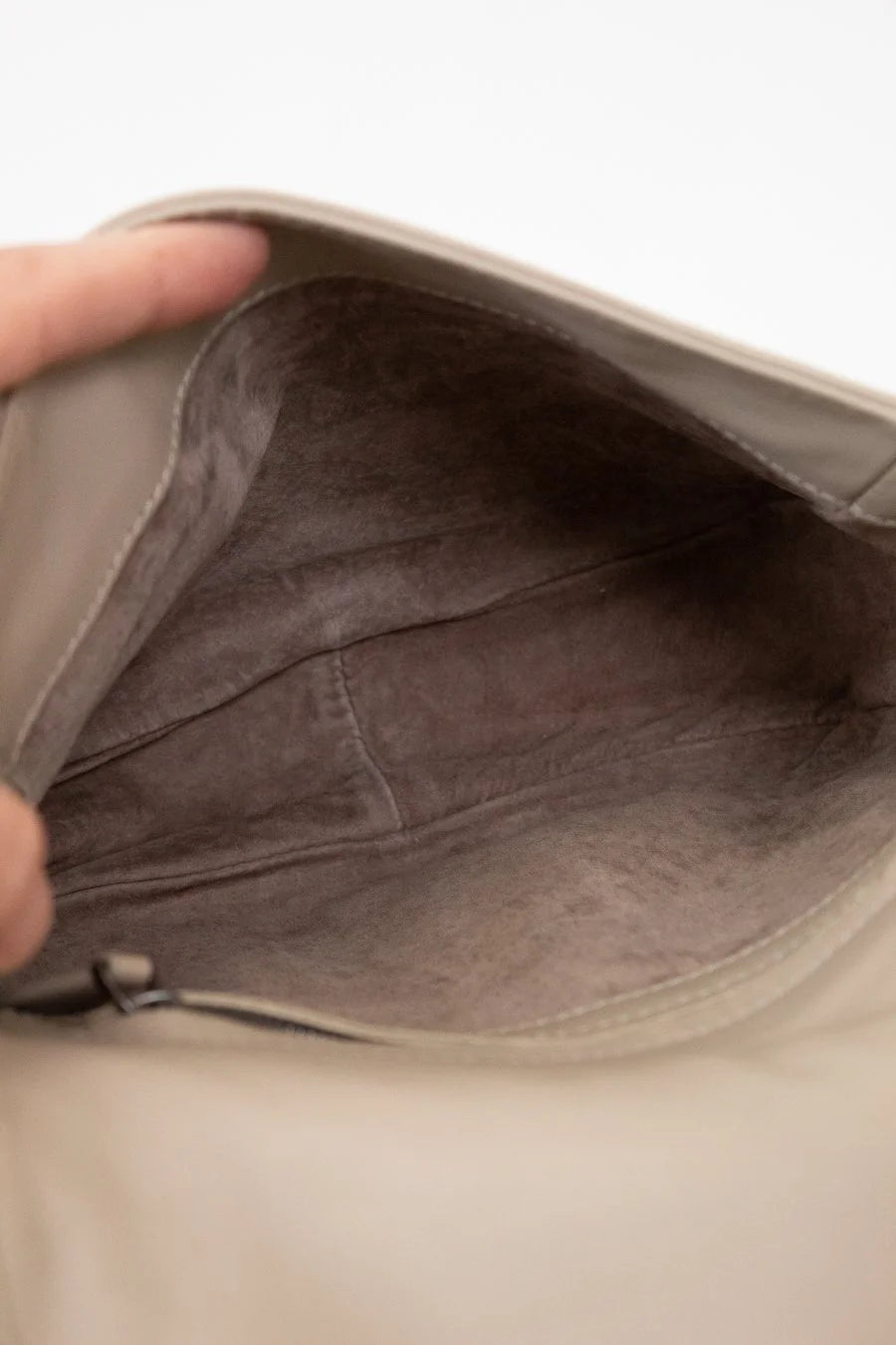 Close-up of a beige leather bag with a hand holding it open.