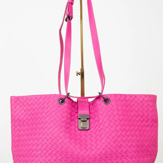 Pink woven handbag on a gold stand on a white background