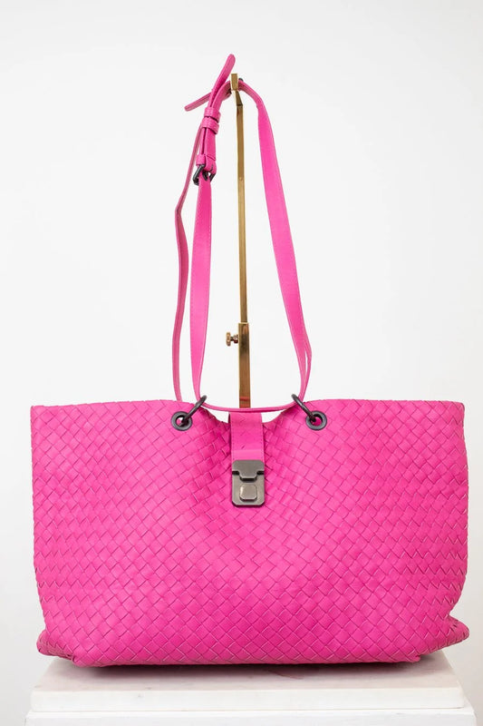Pink woven handbag on a gold stand on a white background