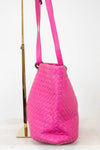 Pink woven handbag with a strap on a white background