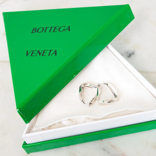 Silver earrings in a Bottega Veneta box on a marble surface