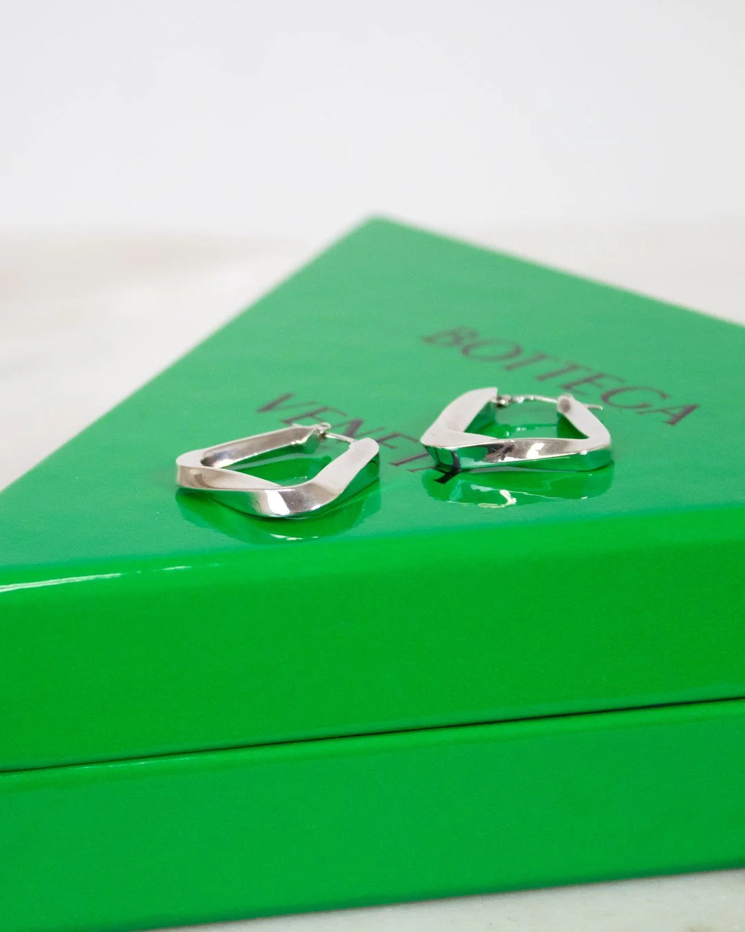 Silver hoop earrings on a green box with 'Bottega Veneta' branding.